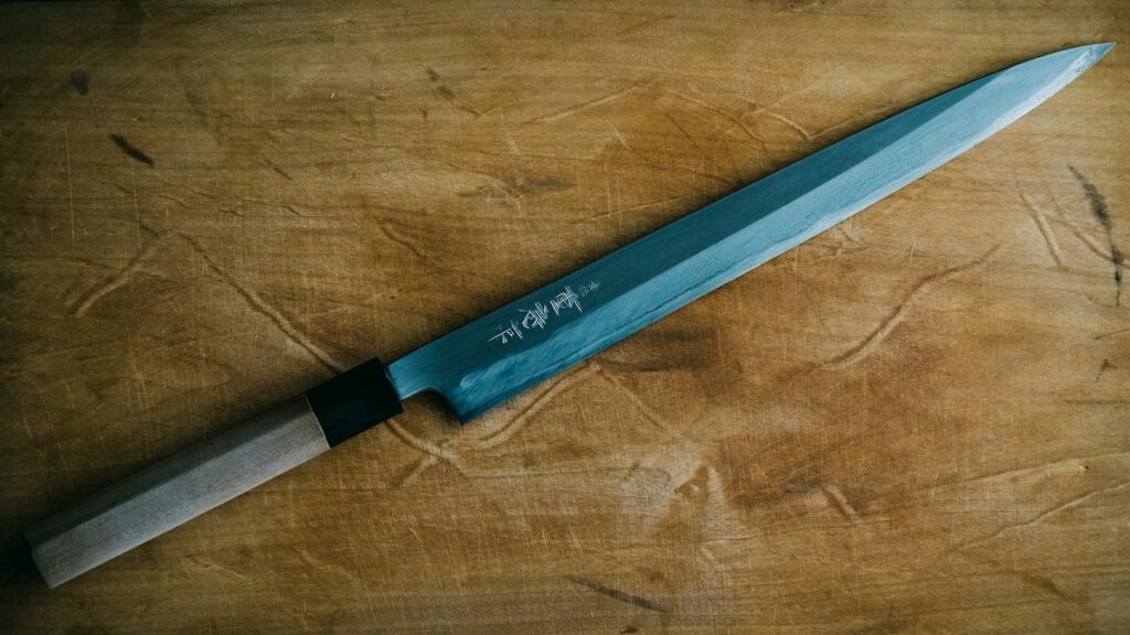 Japanese single bevel yanagiba knife resting on a worn wooden cutting board